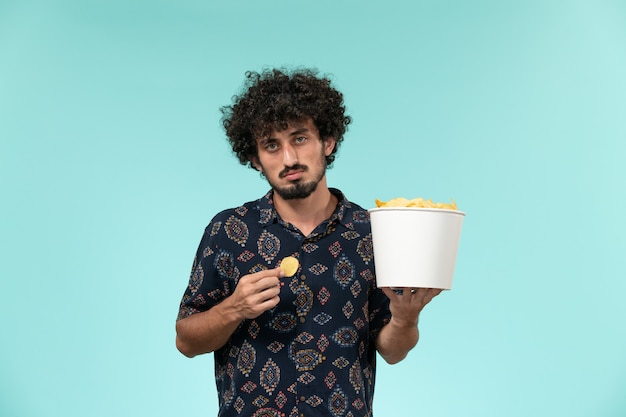 Vista frontale del giovane che tiene il cestino con le patatine fritte e mangia sul maschio del teatro di film di film del cinema della parete blu