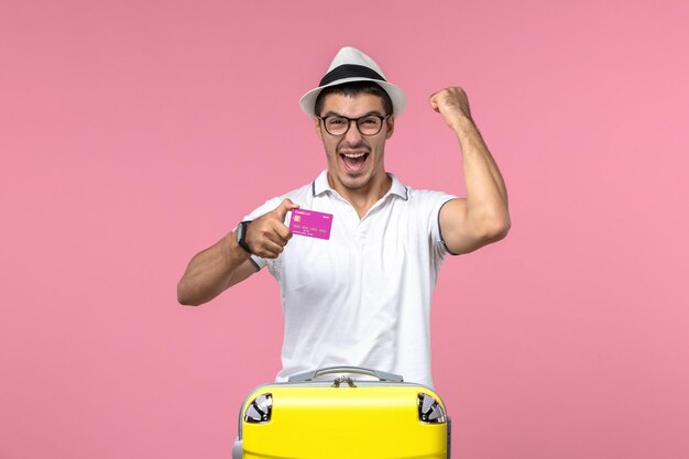Vista frontale del giovane che tiene la carta di credito durante le vacanze estive sulla parete rosa