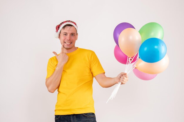 Vista frontale del giovane che tiene palloncini colorati sul muro bianco