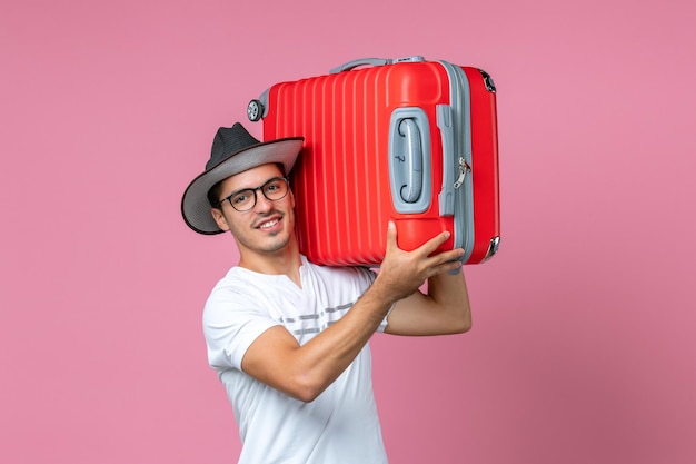 Vista frontale del giovane che va in vacanza e tiene in mano una borsa rossa sul muro rosa