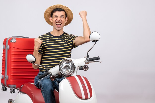 Vista frontale del giovane con cappello di paglia sul ciclomotore che esprime la sua felicità