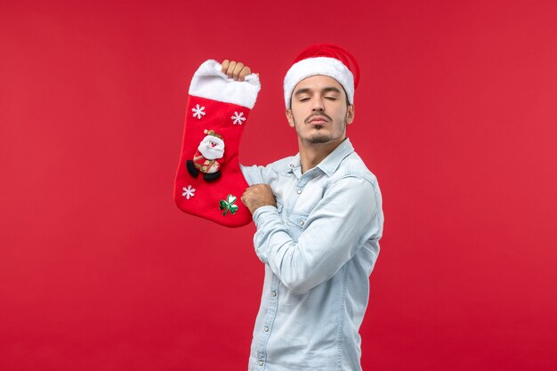 Vista frontale del giovane con il calzino di Natale sulla parete rossa