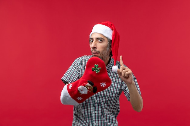 Vista frontale del giovane con il calzino di Natale sulla parete rossa