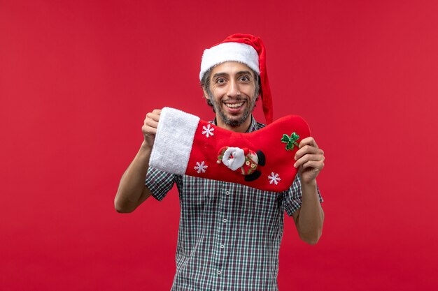 Vista frontale del giovane con il calzino di Natale sulla parete rossa