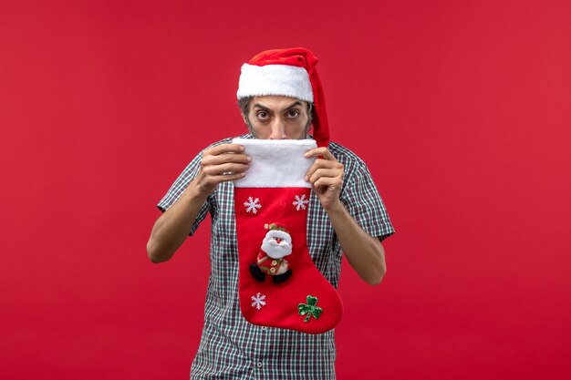 Vista frontale del giovane con il calzino di Natale sulla parete rossa