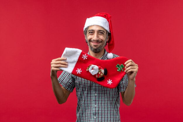 Vista frontale del giovane con il grande calzino di Natale sulla parete rossa