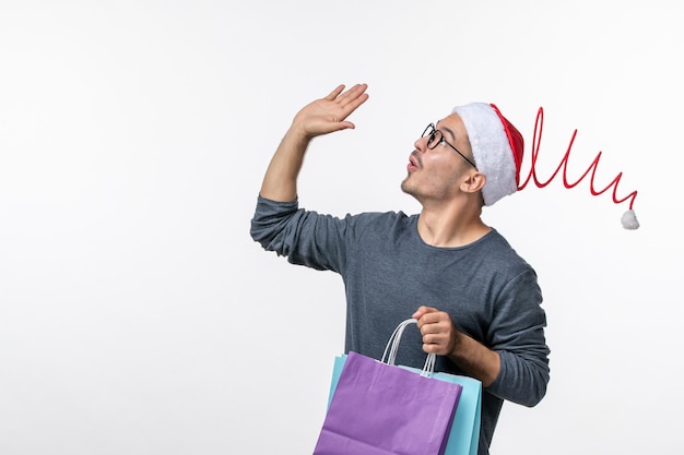 Vista frontale del giovane dopo lo shopping natalizio sul muro bianco