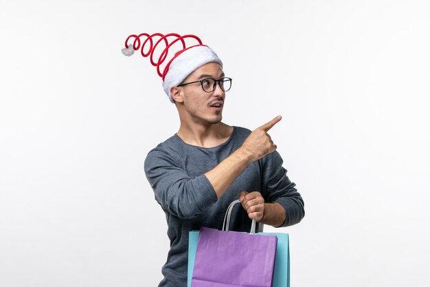 Vista frontale del giovane dopo lo shopping natalizio sul muro bianco