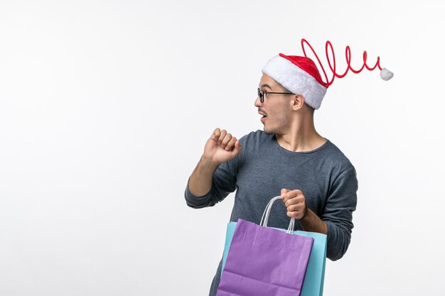 Vista frontale del giovane dopo lo shopping natalizio sul muro bianco