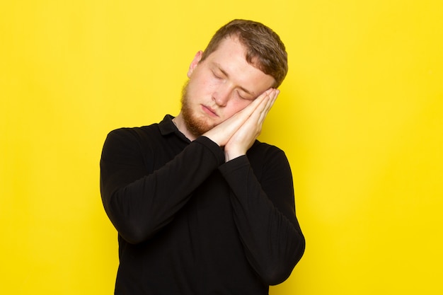 Vista frontale del giovane in camicia nera che posa con il gesto di sonno