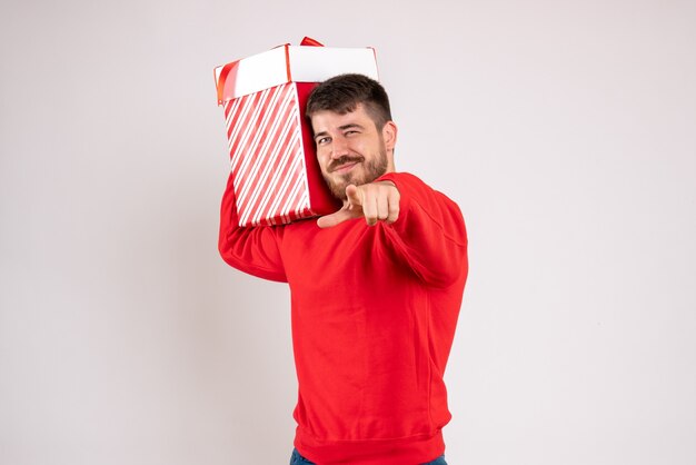 Vista frontale del giovane in camicia rossa che tiene regalo di Natale nella casella sul muro bianco