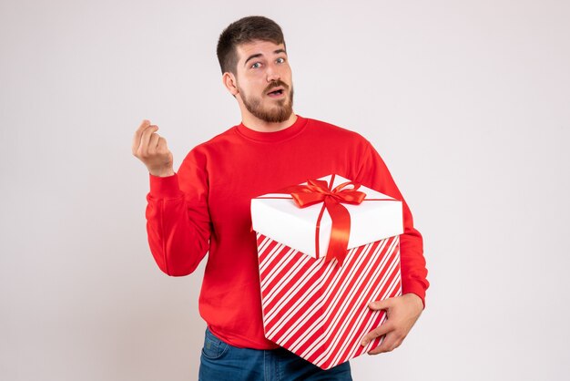 Vista frontale del giovane in camicia rossa che tiene regalo di Natale nella casella sul muro bianco