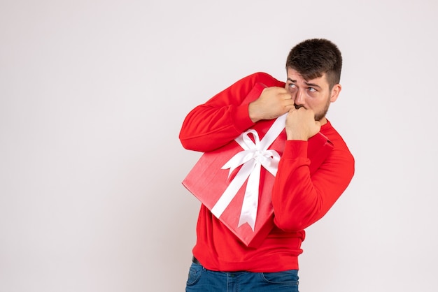 Vista frontale del giovane in camicia rossa che tiene regalo di Natale sulla parete bianca