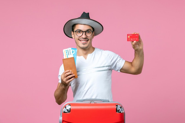 Vista frontale del giovane in possesso di biglietti e carta di credito sul pavimento rosa viaggio estivo uomo viaggio emozione aereo