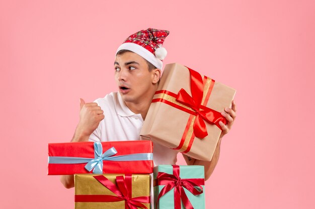 Vista frontale del giovane intorno a diversi regali di Natale sulla parete rosa