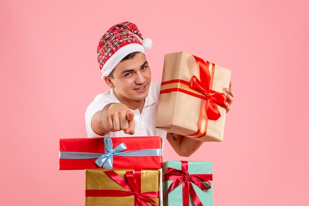 Vista frontale del giovane intorno a diversi regali di Natale sulla parete rosa