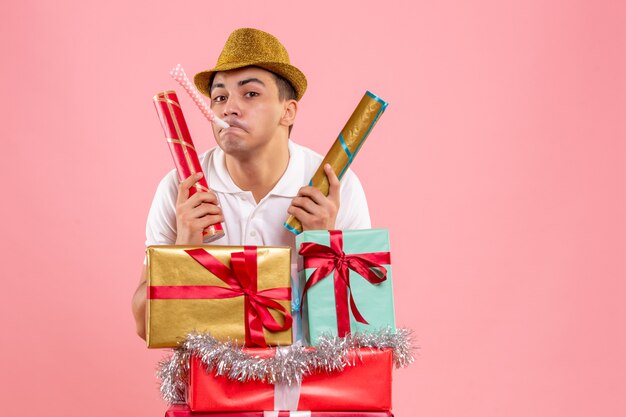 Vista frontale del giovane intorno a regali di Natale con petardi sulla parete rosa