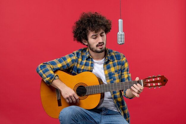 Vista frontale del giovane maschio che suona la chitarra sul colore del concerto del musicista dal vivo del cantante della banda del muro rosso