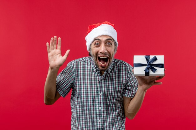 Vista frontale del giovane maschio che tiene il regalo di Natale sul rosso