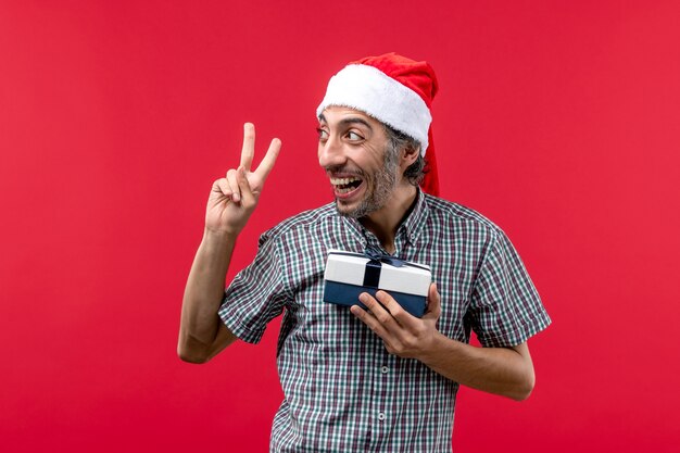 Vista frontale del giovane maschio che tiene un piccolo regalo di Natale sul rosso