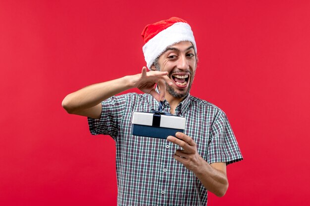 Vista frontale del giovane maschio che tiene un piccolo regalo di Natale sul rosso