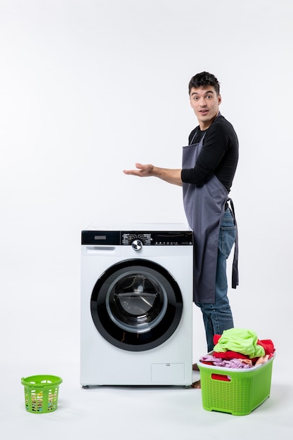 Vista frontale del giovane maschio con vestiti sporchi e lavatrice sul muro bianco