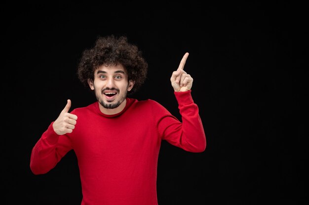 Vista frontale del giovane maschio in camicia rossa sul muro nero