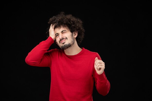 Vista frontale del giovane maschio in camicia rossa sul muro nero