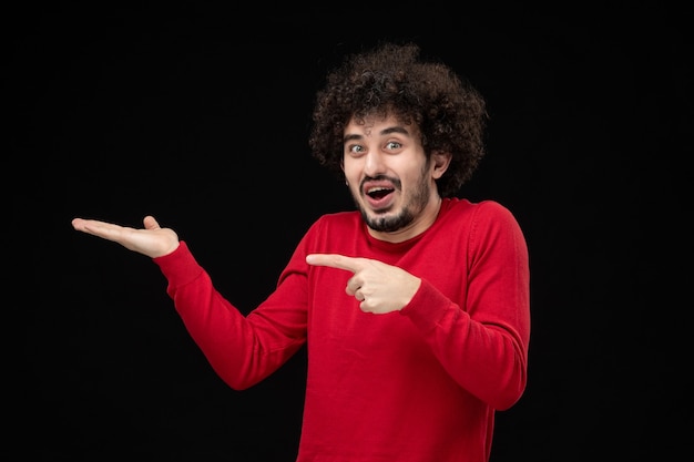 Vista frontale del giovane maschio in camicia rossa sul muro nero