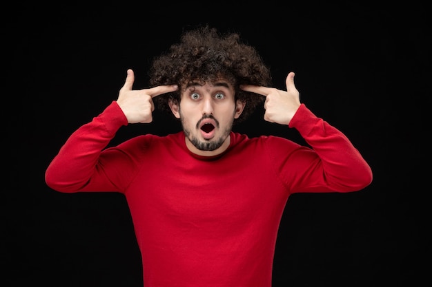 Vista frontale del giovane maschio in camicia rossa sul muro nero