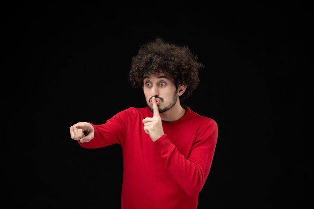 Vista frontale del giovane maschio in maglione rosso sul muro nero