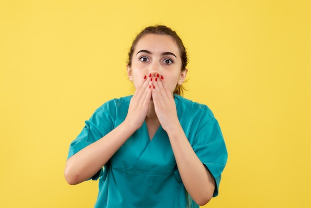 Vista frontale del giovane medico di sesso femminile in tuta medica sulla parete gialla