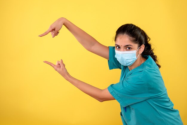 Vista frontale del giovane medico femminile con la maschera sulla parete gialla