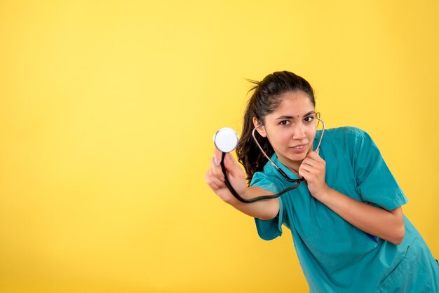 Vista frontale del giovane medico femminile con lo stetoscopio in piedi sulla parete gialla