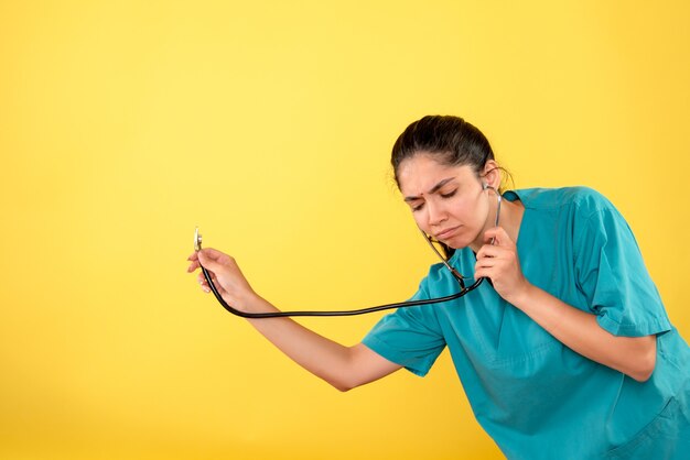 Vista frontale del giovane medico femminile con lo stetoscopio sulla parete gialla