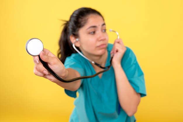 Vista frontale del giovane medico femminile con lo stetoscopio sulla parete isolata gialla