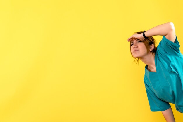 Vista frontale del giovane medico femminile guardando a distanza sulla parete gialla