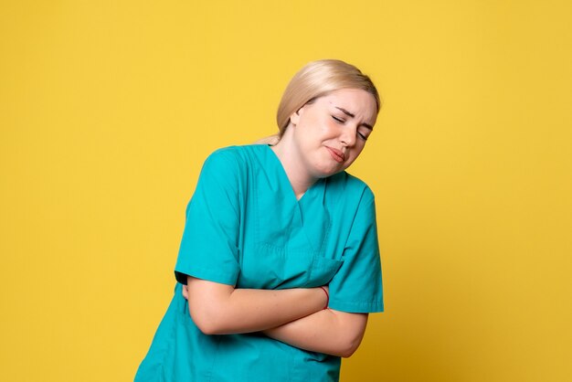 Vista frontale del giovane medico femminile in camicia medica che soffre di mal di stomaco sulla parete gialla