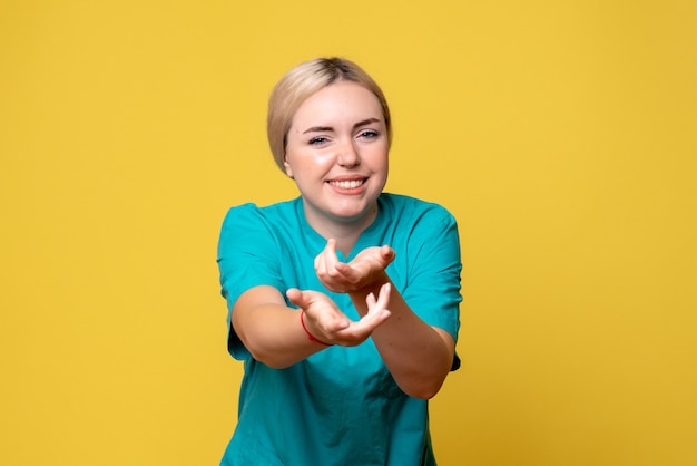 Vista frontale del giovane medico femminile in camicia medica con braccio ferito sulla parete gialla