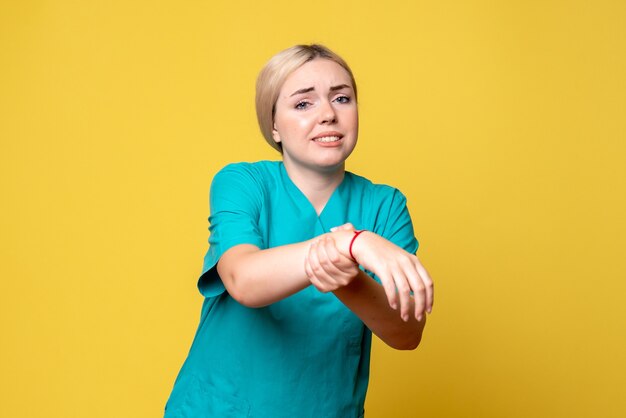 Vista frontale del giovane medico femminile in camicia medica con la mano ferita sulla parete gialla