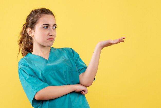 Vista frontale del giovane medico femminile in camicia medica sulla parete gialla