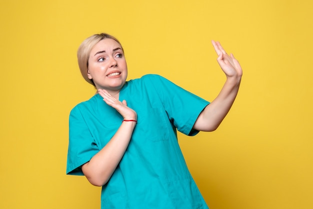 Vista frontale del giovane medico femminile in camicia medica sulla parete gialla