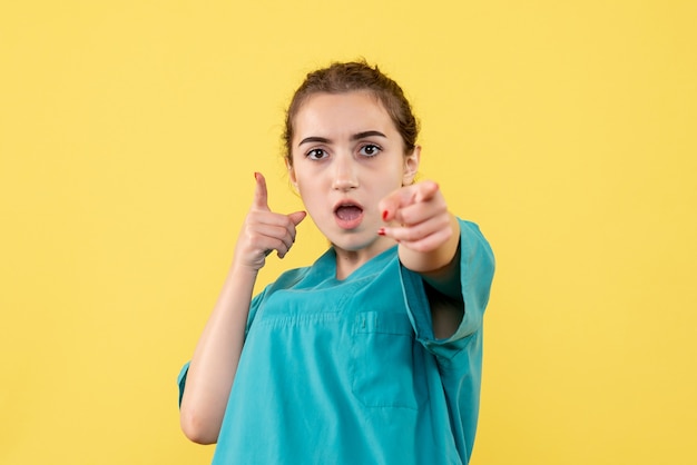 Vista frontale del giovane medico femminile in camicia medica sulla parete gialla