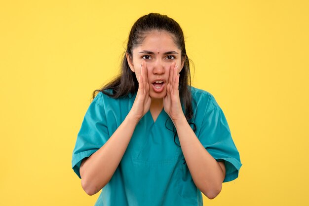 Vista frontale del giovane medico femminile in uniforme che chiama qualcuno sulla parete gialla