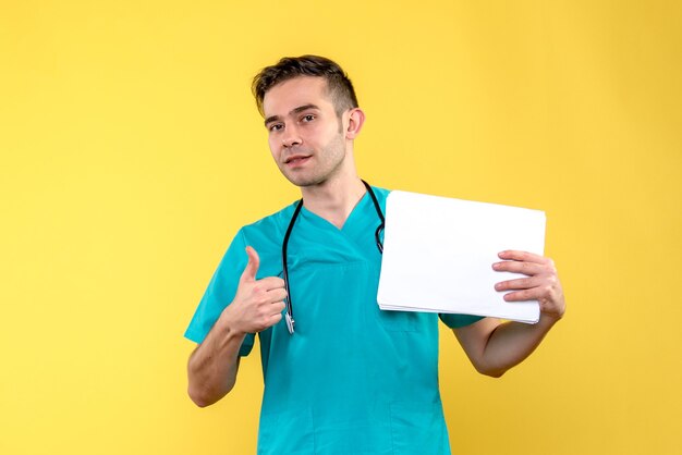 Vista frontale del giovane medico maschio con documenti sul virus della salute covid pavimento giallo