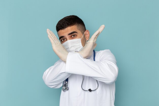 Vista frontale del giovane medico maschio in abito bianco con stetoscopio blu che indossa una maschera sterile