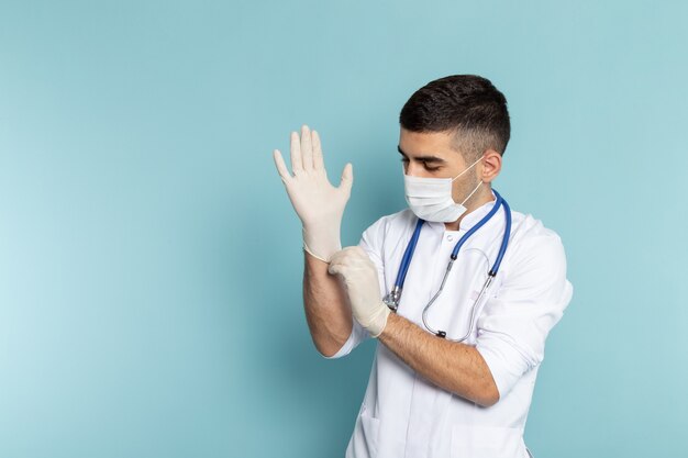 Vista frontale del giovane medico maschio in abito bianco con stetoscopio blu sorridente indossando guanti
