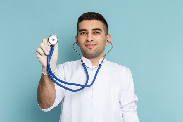 Vista frontale del giovane medico maschio in abito bianco con stetoscopio blu sorridente