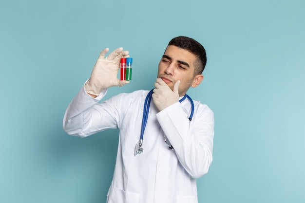 Vista frontale del giovane medico maschio in abito bianco con stetoscopio blu tenendo le boccette