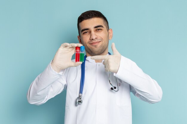 Vista frontale del giovane medico maschio in vestito bianco con lo stetoscopio blu che tiene le boccette con il sorriso